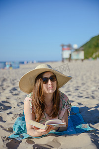 一个年轻的黑发女人在沙滩上放松、看书的画像