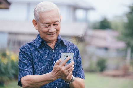 使用智能手机的愉快的亚裔老人。