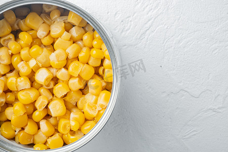 蔬菜平铺摄影照片_锡罐中的甜玉米粒，白色背景，顶视图平铺，带有文本复制空间