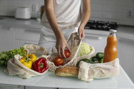 女人的手，拿着一个可重复使用的食品袋，在家里的厨房里放着蔬菜，把西红柿拿出来。