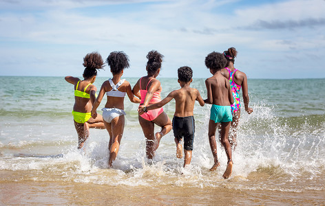 沙滩上的孩子摄影照片_孩子们在沙滩上的沙滩上玩耍，一群孩子在夏天手牵着手在沙滩上排成一排，后视大海和蓝天