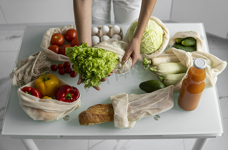 食品袋摄影照片_女人的手，拿着一个可重复使用的食品袋，在家里的厨房里放着蔬菜，把沙拉拿出来。