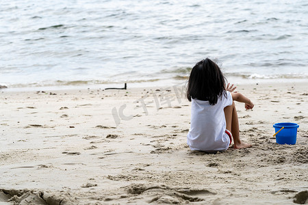 小女孩坐在沙滩上的沙滩上，独自看着大海