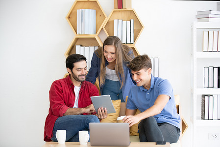 在办公室工作的商务人士使用台式电脑，一群穿着时髦休闲装的快乐商务人士看着笔记本电脑并打手势。
