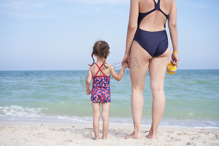 后面摄影照片_母女一起海滩后视镜 无法辨认的白种女人小女孩泳装站在海边后面。