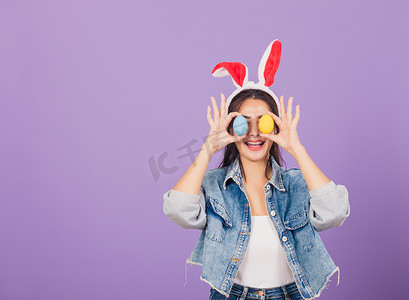 眼耳摄影照片_微笑的女人戴着兔耳和牛仔布，前眼拿着五颜六色的复活节彩蛋