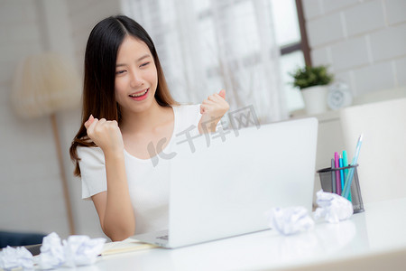 年轻的亚洲女性自信地在家里用笔记本电脑工作，思考规划的想法，自由快乐的女孩表达兴奋和成功，使用笔记本思想，商业理念。