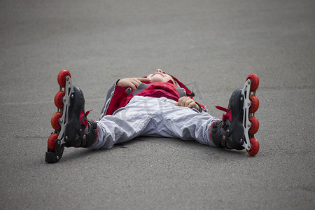 穿着溜冰鞋的男孩躺在人行道上。穿着溜冰鞋的孩子摔倒了