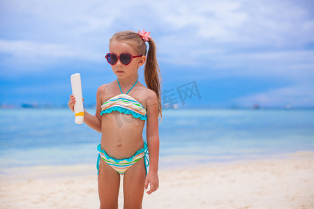 泳装的小可爱女孩拿着晒黑化妆水瓶
