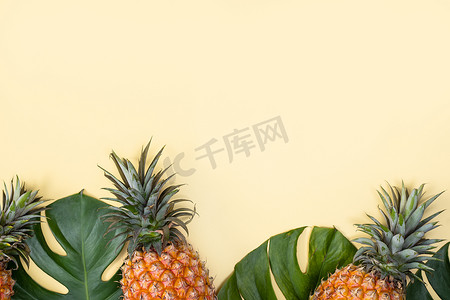 热带棕榈蒙斯特拉叶上的美丽菠萝与明亮的淡黄色背景、顶视图、平躺、头顶上方的夏季水果隔离开来。