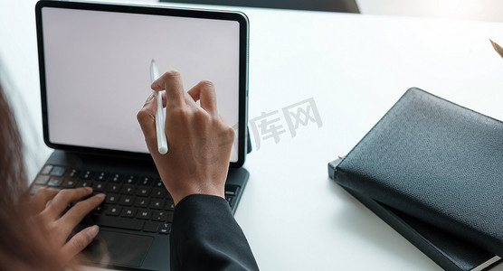 在现代办公室里，女商人用手写笔在数字平板电脑上用笔记本电脑工作。
