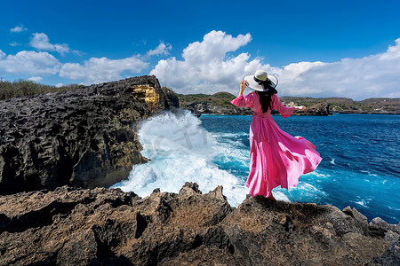 美丽的女孩站在 Angels Billabong 的岩石上，靠近印度尼西亚巴厘岛努沙佩尼达岛的破碎海滩。
