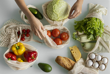 食品袋摄影照片_女人的手，拿着一个可重复使用的食品袋，在家里的厨房里放着蔬菜，把西红柿拿出来。