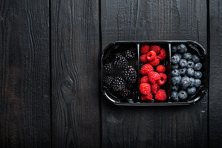 浆果盛肉盘，浆果、蓝莓、覆盆子和黑莓的收获，顶视图，在黑色木桌上
