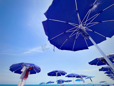 阳光明媚的夏日，意大利海滩上的蓝色太阳伞打开并排成一排