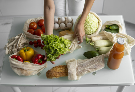 女人的手，拿着一个可重复使用的食品袋，在家里的厨房里放着蔬菜，把沙拉拿出来。