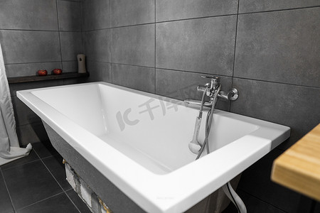浴室内部墙上贴着灰色瓷砖，时尚的白色浴缸配有银色水龙头。