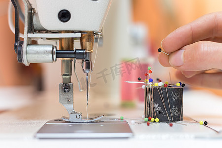 裁缝车间的缝纫机和针：特写裁缝手拿着针