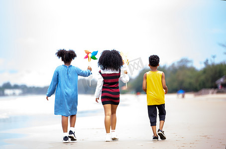 孩子们在沙滩上的沙滩上玩耍，一群孩子在夏天手牵着手在沙滩上排成一排，后视大海和蓝天