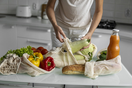 女人的手，拿着一个可重复使用的食品袋，在家里的厨房里放着蔬菜，把西葫芦拿出来。