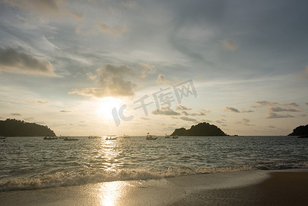 日落天空的景色和漂浮的小船和海滩上的小岛的轮廓