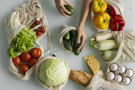 女人的手，拿着一个可重复使用的食品袋，在家里的厨房里放着蔬菜，把黄瓜拿出来。