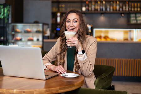 女商人餐厅老板在餐厅使用笔记本电脑穿着优雅的裤装坐在桌子上与酒吧柜台背景