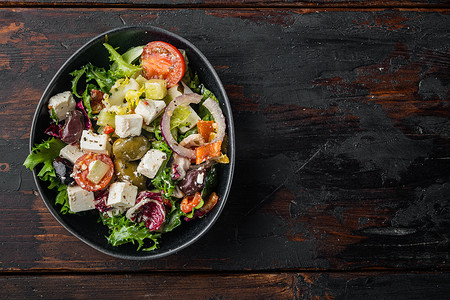 希腊沙拉配新鲜蔬菜、菲塔奶酪和橄榄，在旧的深色木桌背景上，顶视图平铺着文字复制空间