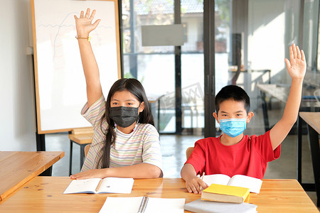 戴口罩的女男孩学生在课堂上举手学习。