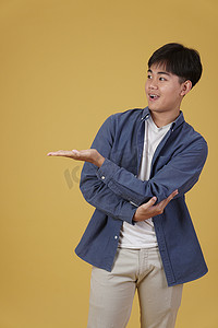 黄色手指手势摄影照片_快乐英俊的亚洲年轻男子的肖像，穿着随意，在黄色背景中隔离的复制空间中用张开的手掌手势呈现