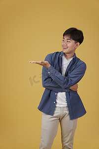 快乐英俊的亚洲年轻男子的肖像，穿着随意，在黄色背景中隔离的复制空间中用张开的手掌手势呈现