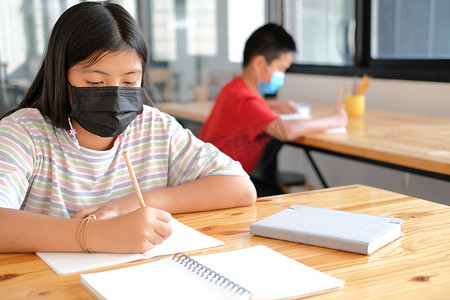 戴着口罩学习写笔记做作业的女学生。