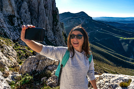 白人年轻女性在山顶张开嘴用智能手机自画像，背景全景美丽 — 单身女性旅行者利用互联网技术分享她的自然之旅