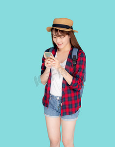 手机夏季夏季摄影照片_美丽的年轻亚洲女性在度假时触摸智能手机，与世隔绝在蓝色背景下，亚洲女孩在夏季旅行、旅行或教育概念中在智能手机上聊天或聊天。
