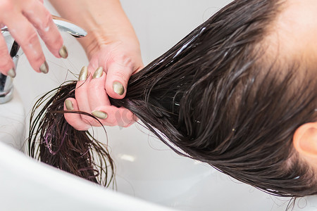 美发师在水槽里给一个长头发的女孩洗头。