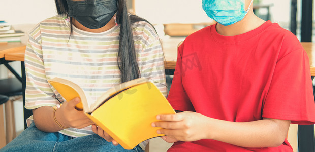 戴口罩的男孩女孩学生在图书馆读书。