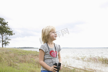 女孩站在湖边用双筒望远镜