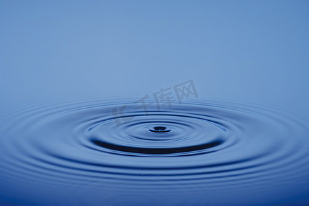 特写水滴或飞溅落在水面上，美丽的圆波纹，水概念，蓝色背景