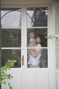 母亲和蹒跚学步的孩子站在一扇带玻璃窗的门内