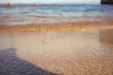 金色的沙滩被清晨的阳光照亮的海水冲刷，低角度特写细节 — 抽象的浅景深海洋背景，只有很少的颗粒在焦点
