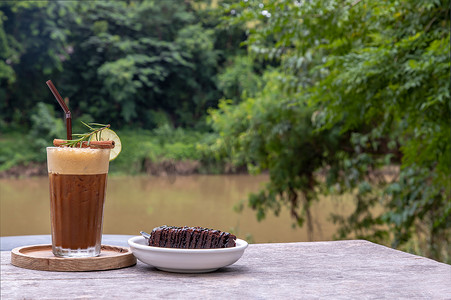 蜂蜜柠檬咖啡配巧克力布朗尼蛋糕，木制背景，可欣赏河景。
