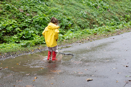 下雨时穿着黄色雨衣跳水坑的嬉戏女孩