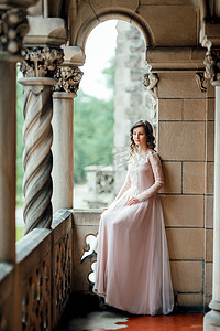 中世纪城堡背景下穿着浅粉色连衣裙的女孩