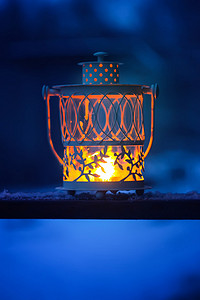 大气冬季背景摄影照片_冬季公园白雪覆盖的冷杉树枝上挂着燃烧蜡烛的装饰圣诞灯笼。