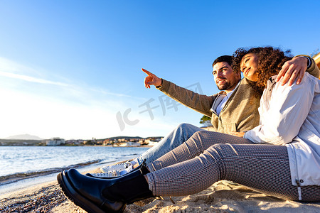 深情相爱的年轻情侣坐在靠近海水的海边，紧挨着看着日落。