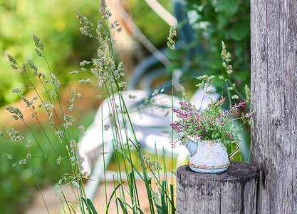 花园秋千背景上带野花的老式小乡村茶壶