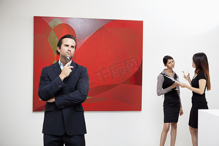 盛事摄影照片_年轻男子与两个女人在艺术画廊的背景下思考