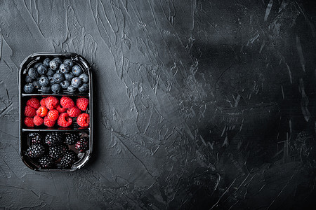 市场托盘中的成熟浆果、蓝莓、覆盆子和黑莓，顶视图，带复制空间，黑色背景