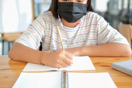 儿童口罩摄影照片_戴着口罩学习写笔记做作业的女学生。