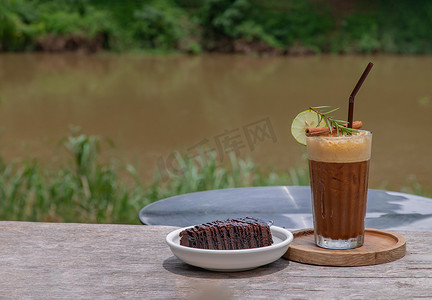 蜂蜜柠檬摄影照片_蜂蜜柠檬咖啡配巧克力布朗尼蛋糕，木制背景，可欣赏河景。